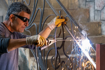 Man wearing protective glasses welds metal with welding machine. sparks from welding fly to sides. 