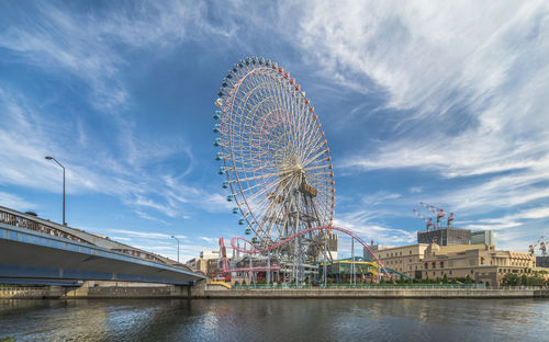 Ferris wheel by river against sky in city