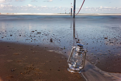 Wet glass bottle on beach against sky