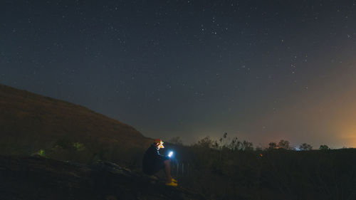 Man using mobile phone while sitting on mountain against sky at dusk