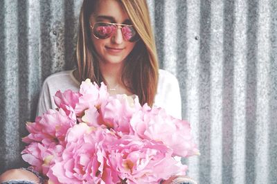 Portrait of smiling young woman standing by pink flowers