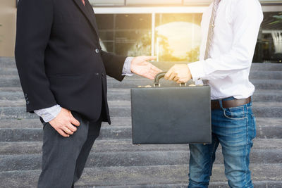 Midsection of businessman giving suitcase to man on steps