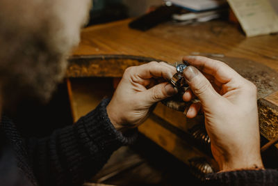 Anonymous jeweler holding unfinished ring in dirty hands and checking quality in workshop