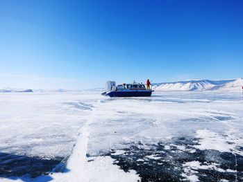 People on frozen lake against clear blue sky