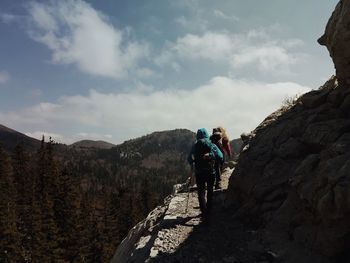 Rear view of hiker walking on mountain against cloudy sky