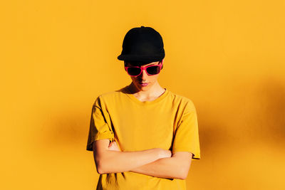 Young man wearing sunglasses standing against yellow background