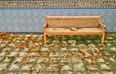 Empty bench on footpath covered with fallen dry leaves