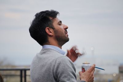 Close-up of man holding ice cream against sky