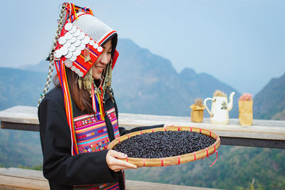 Midsection of woman holding hat against mountains