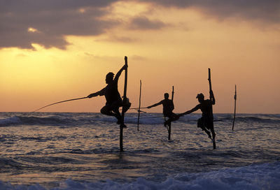 Silhouette fishermen stilt fishing in sea during sunset