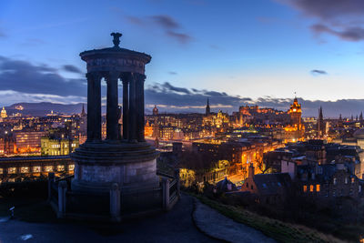 Illuminated buildings in city against sky at sunset