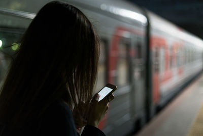 Rear view of woman using mobile phone on subway platform