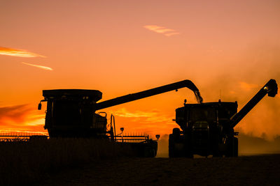 Silhouette combine harvester on land against sky during sunset