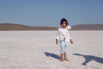 Child a boy in a white shirt stands on a large dried up salt lake in the summer in the crimea