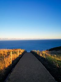 Road by sea against clear blue sky