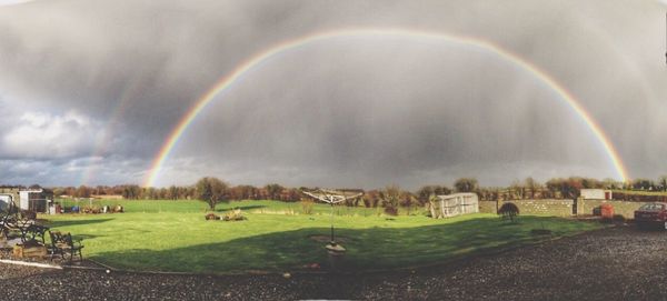 Rainbow over field against cloudy sky