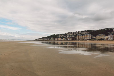 Scenic view of beach by buildings against cloudy sky