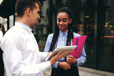 Young man holding smart phone while standing on laptop