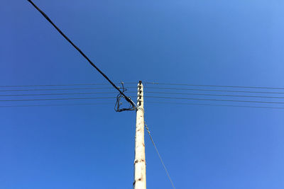 Low angle view of electricity pylon against clear blue sky