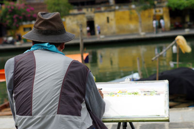 Rear view of artist painting at riverbank