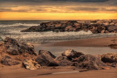 Rocks on beach against sky during sunset