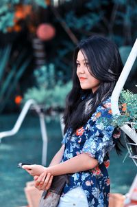 Side view of young woman using phone while leaning on railing