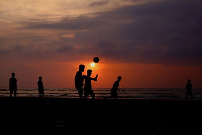 Silhouette people playing on beach against sky during sunset