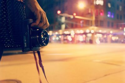 Cropped hand of person holding camera on street in illuminated city