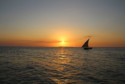 Silhouette sailboat sailing on sea against clear sky during sunset