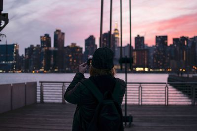 Rear view of woman photographing illuminated buildings in city at dusk