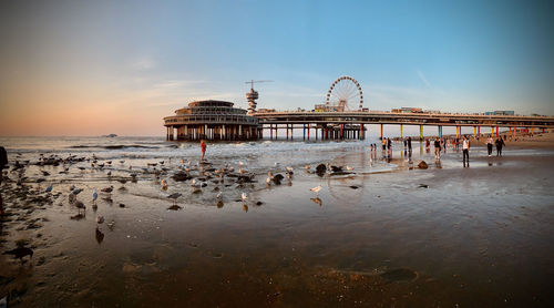 Group of people on pier at beach during sunset