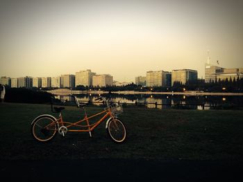 Bicycles parked by river in city against clear sky