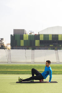 Side view of man sitting on grass against building