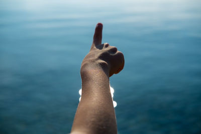 Close-up of hand pointing against sea