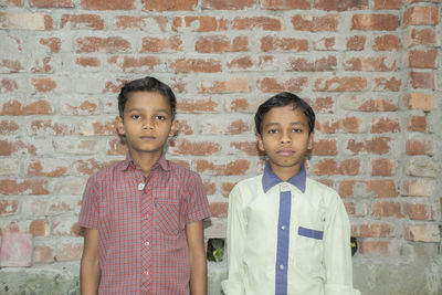 Portrait of boys standing against brick wall