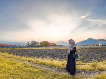 Woman standing on field against sky during sunset