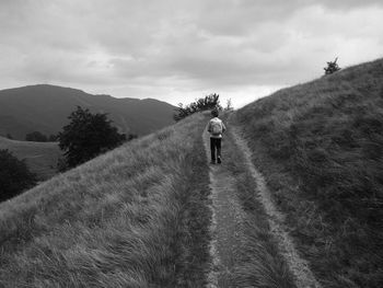 Rear view of man walking on street amidst mountains against sky