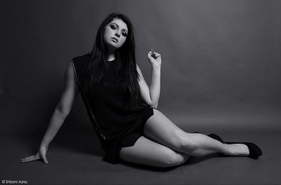 Portrait of a young woman sitting against gray background