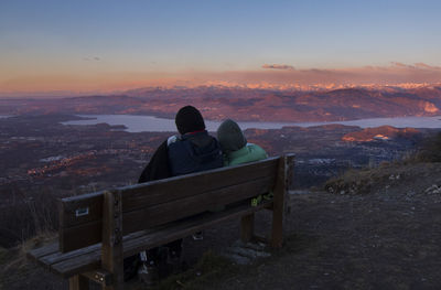 Rear view of men sitting on landscape against sky during sunset