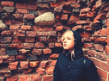 Girl looking away against brick wall