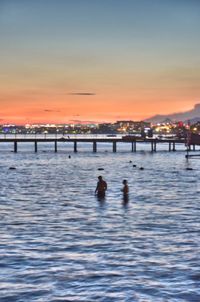 Silhouette people swimming in sea against sky at sunset