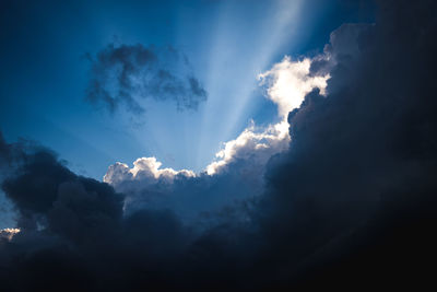 Low angle view of sunlight streaming through clouds