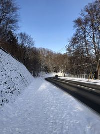 Snow covered road amidst trees against sky