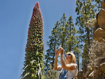 Woman photographing by mobile phone against clear sky