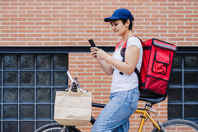 Rider woman wearing red backpack delivering food on bike, checking order on smart phone. delivery