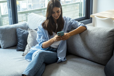 Young woman using mobile phone while sitting on sofa at home