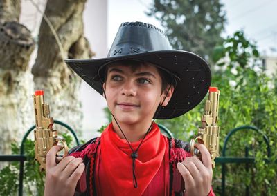 Close-up of boy in cowboy costume holding toy guns at yard