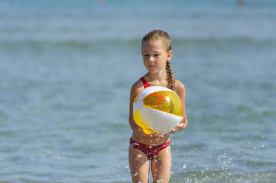 Smiling girl with ball running on beach
