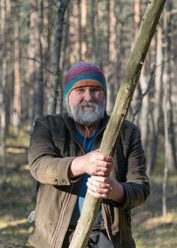 Photo with a portrait of a bearded man in the woods, knitted rough sweater, blurred background