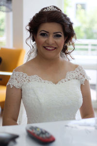 Portrait of smiling bride wearing dress sitting indoors